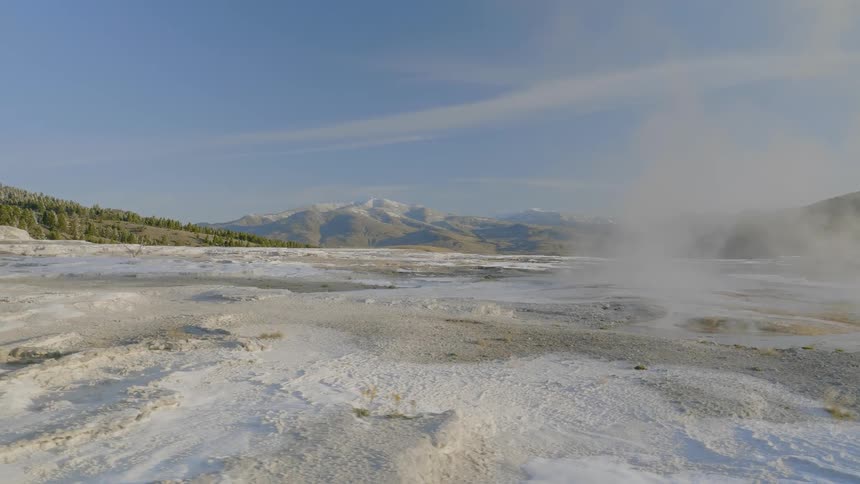 Steam and vapor rise upwards from hot pools of water at a natural spring that is surrounded by mineral deposits