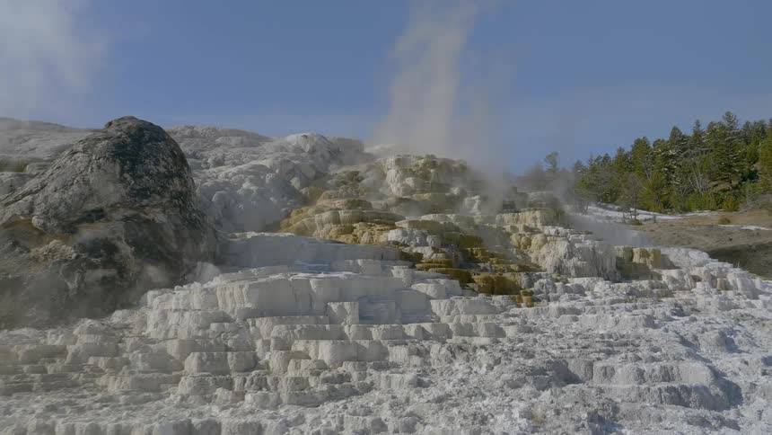 A geyser on a cliff with trees and the sky in the background