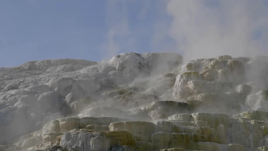 Steam and vapor rise into the air above a group of mineral deposits that surround a natural hot spring