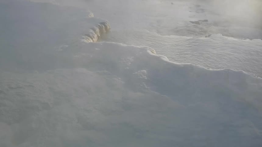 The ice is melting giving off steam near the hot spring
