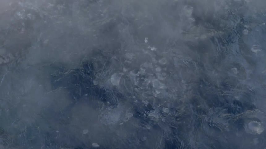 Water is boiling and bubbles emerge from the surface as a copious amount of steam is given off of the surface of the water