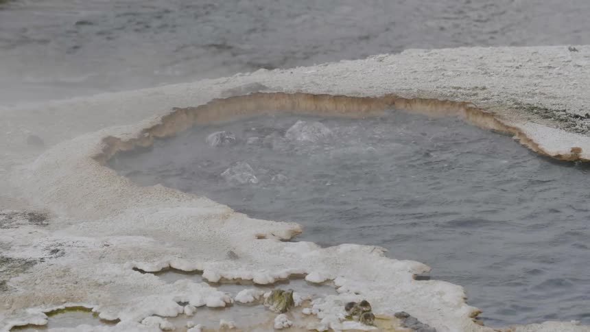 Water bubbles at the surface of a natural hot spring that is surrounded by its mineral encrusted banks