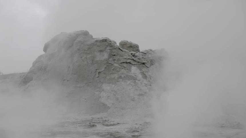 Steam rises from the ground in front of a large rock