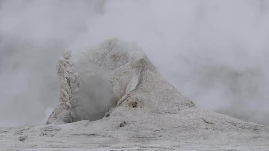 Large clouds of steam billow upwards from a rock formation nearby to a natural hot spring