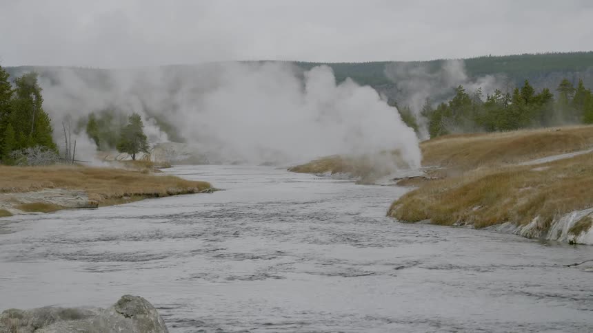 Steam erupts out of geysers and a river flows