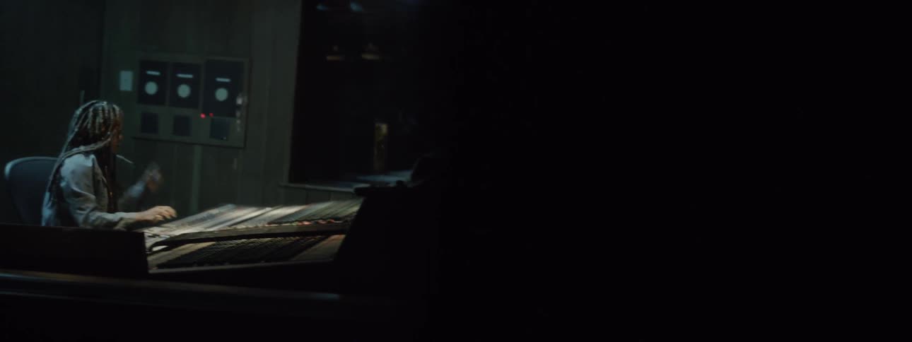 A black female with long dreadlocks is making adjustments to a large music soundboard in a studio