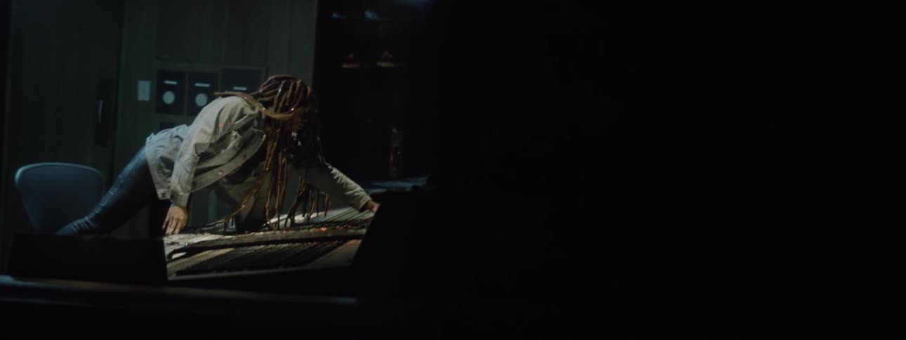 A person with dreadlocks leans over a mixing desk and edits settings