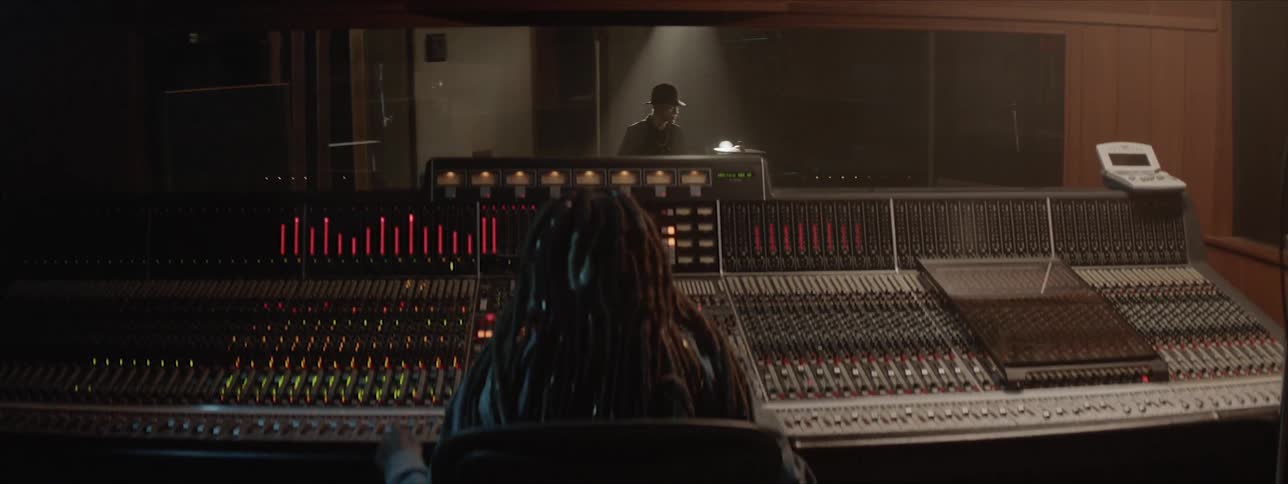 A man plays the drums while a woman works on the sound board
