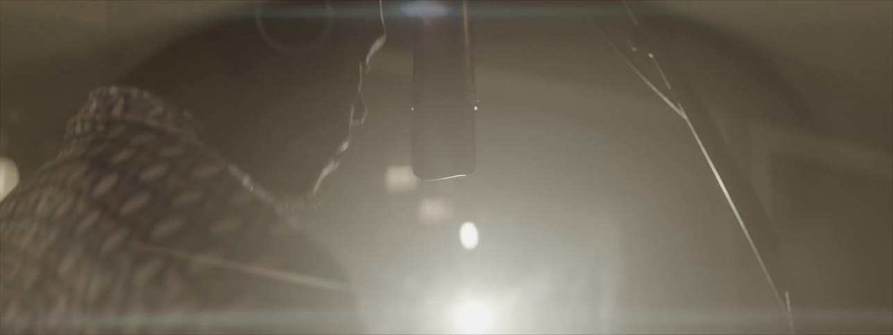 A black man wearing headphones stands in front of a microphone in a recording studio as he bobs and dances to music