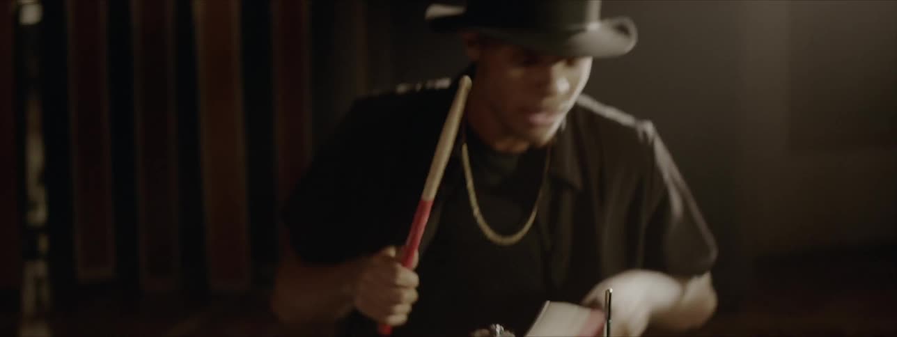 A man indoors playing drums with a black hat and shirt