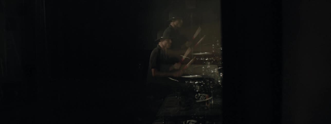 Black drummer wearing black hat plays drums at the stage