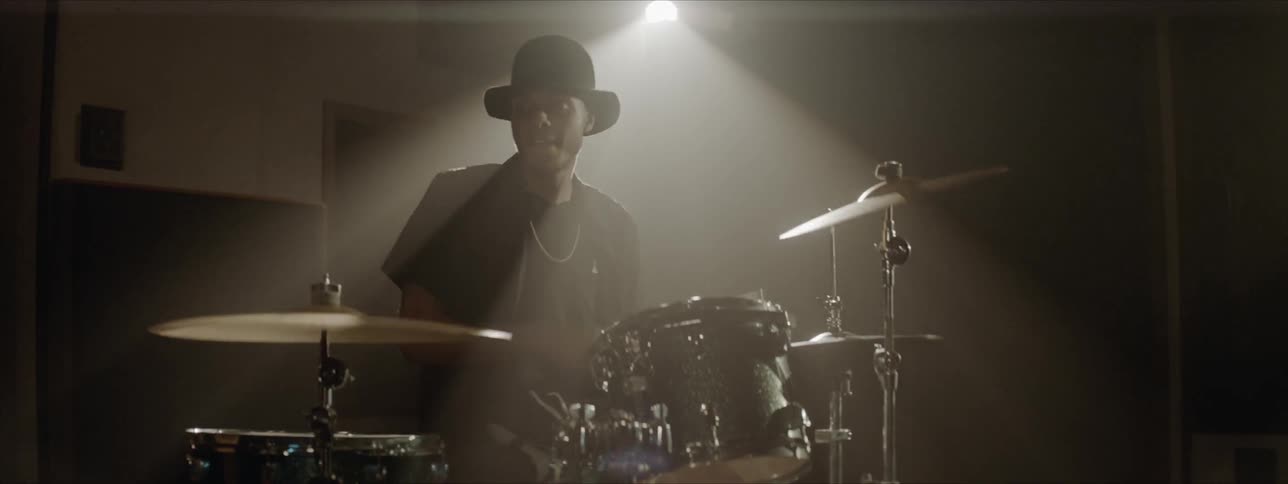 Black drummer wearing black hat plays drums at the stage