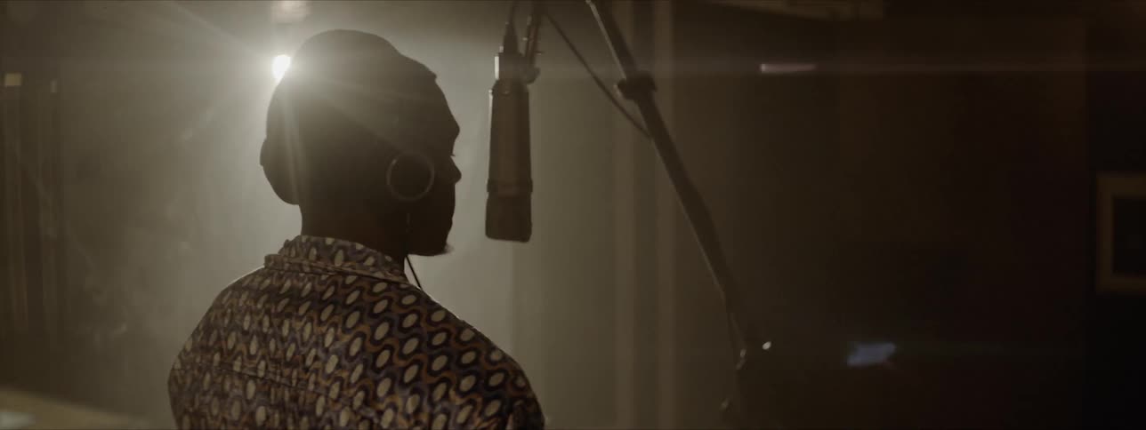 A man in a studio with headphones dancing in front of a mic