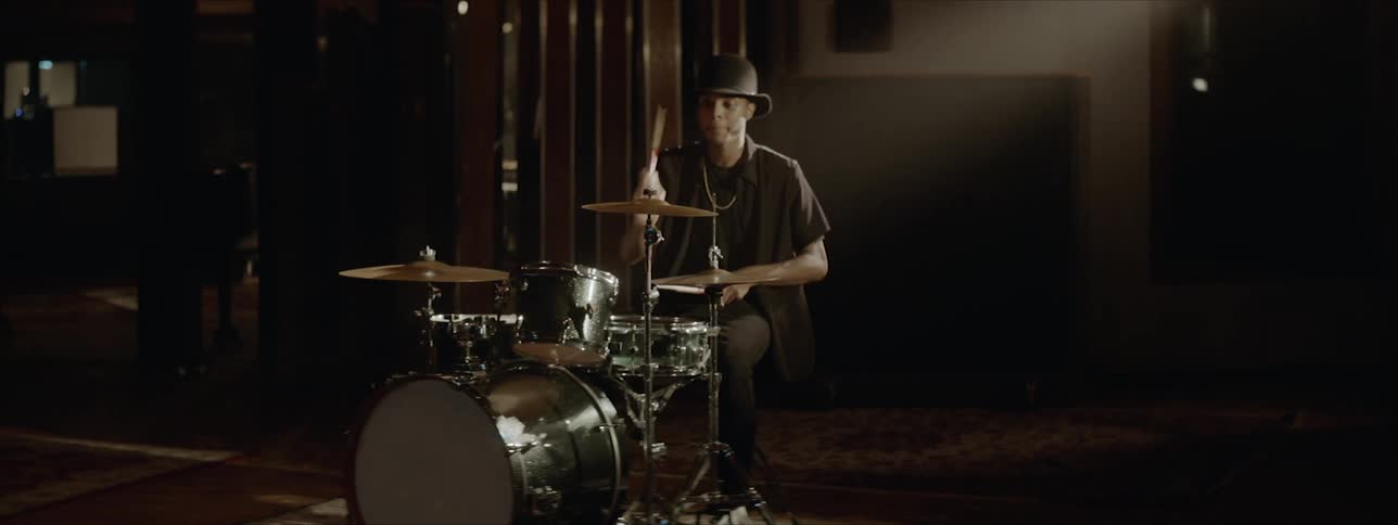 A young black man plays the drums