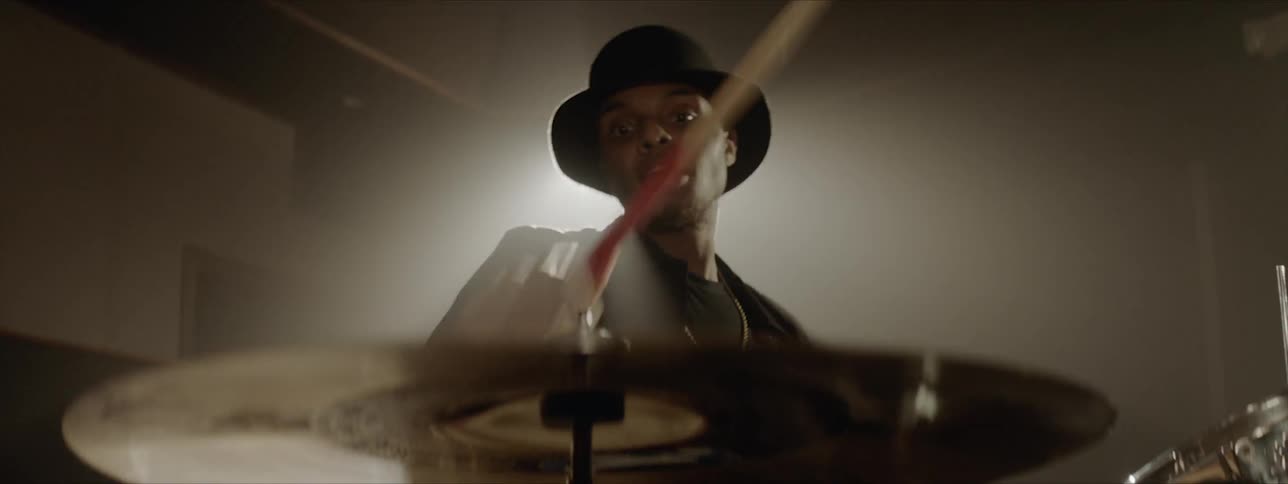 Black man wearing black hat plays drums at stage