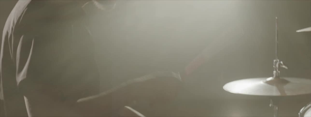 Black man wearing black hat plays drums when the light shines through at stage