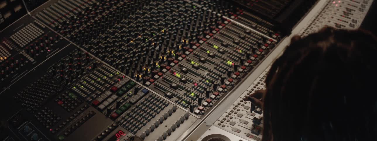 A woman with braids reaches forward and adjusts music studio recording levels