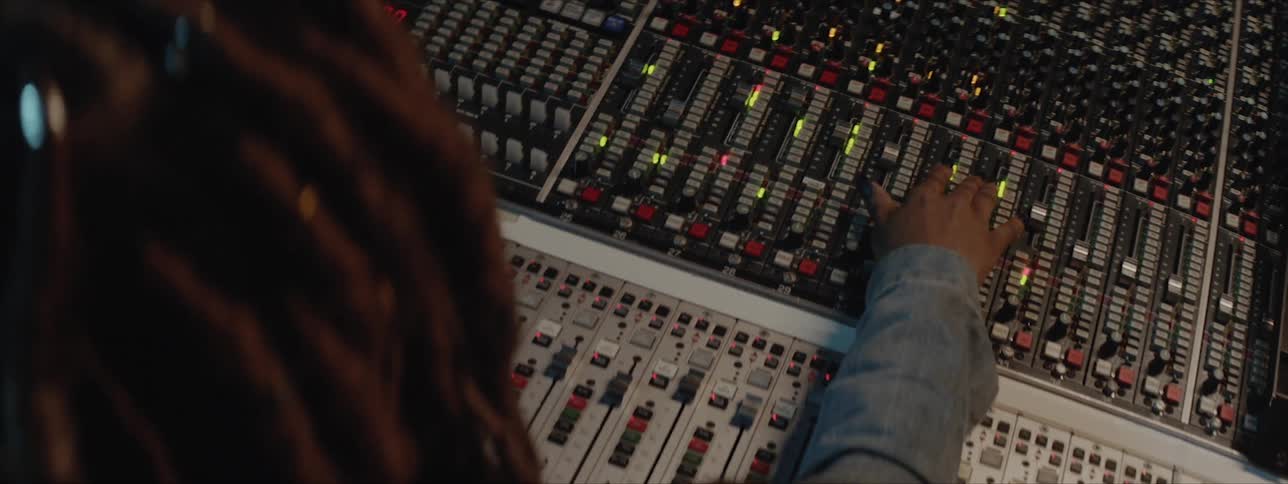 A black woman with long dreadlocks is adjusting slider positions on a large soundboard