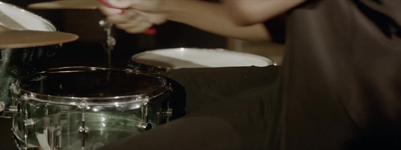 A man wearing a necklace and collared shirt is drumming