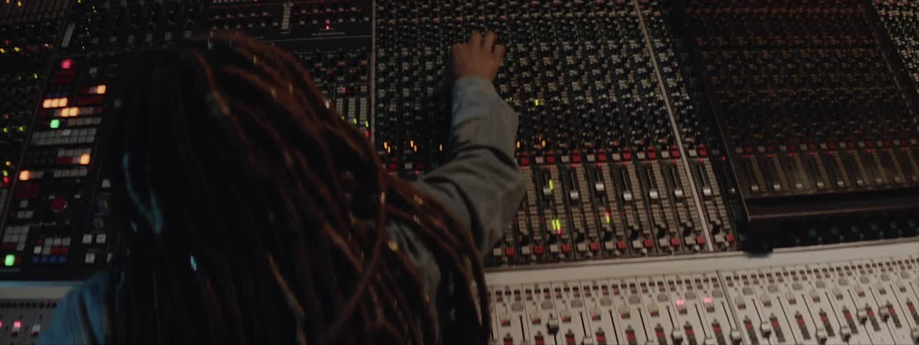 A black female with long dreadlocks is making adjustments to settings on a music soundboard