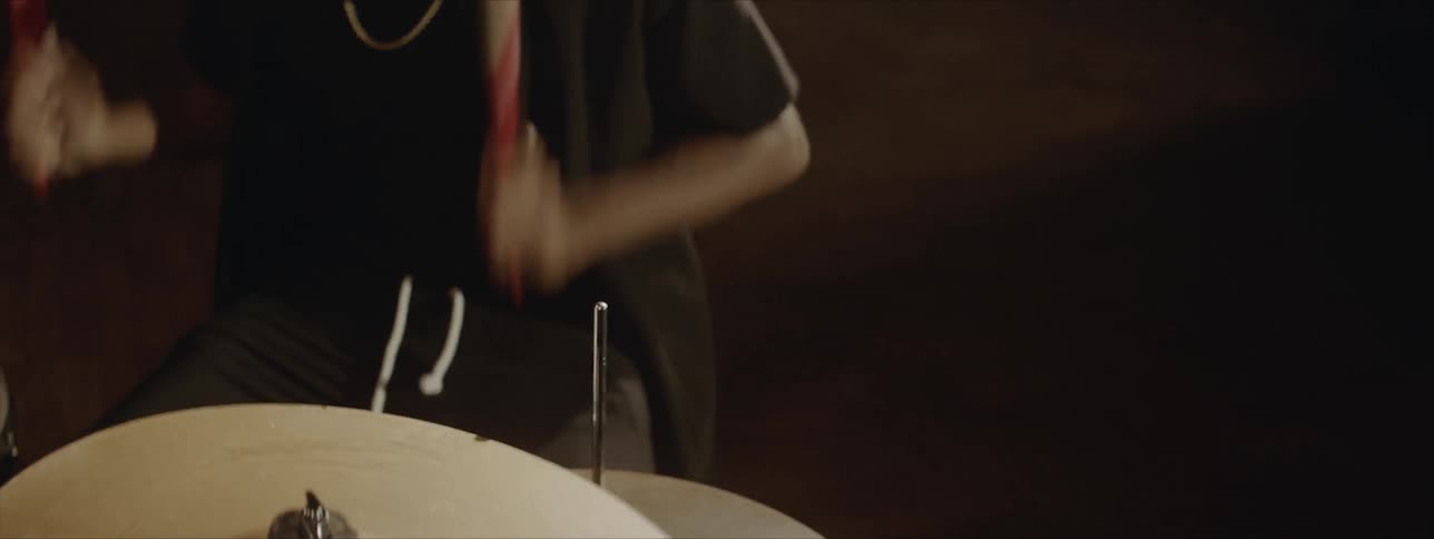 Black drummer wearing black hat plays drums at the stage