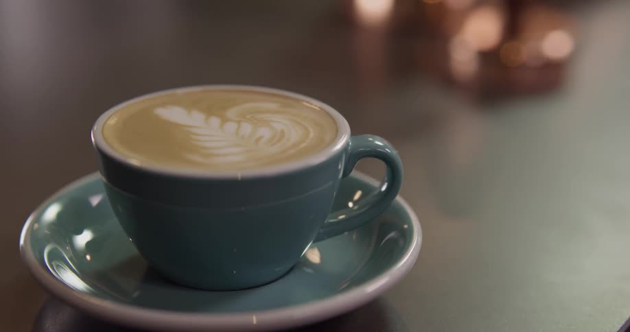 A small coffee cup containing an espresso beverage on a saucer is placed on a counter top briefly and then picked up