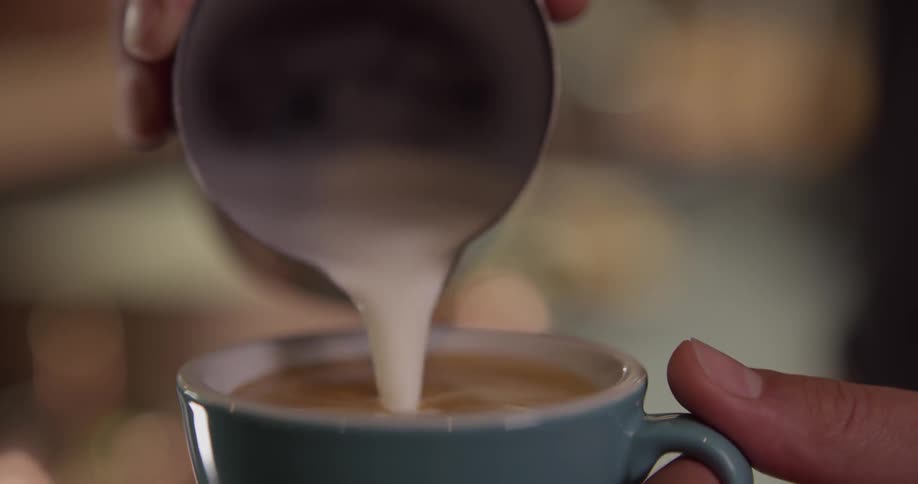 Cream is being poured from a black creamer into coffee in a blue cup