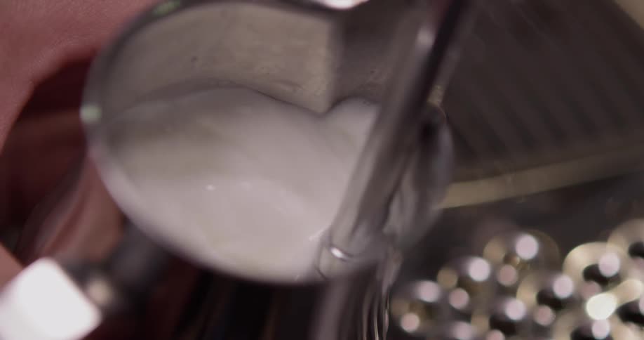 Milk in a metal pot is being foamed with a machine