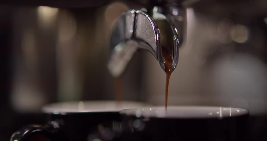 Coffee drips out of a machine in to two mugs