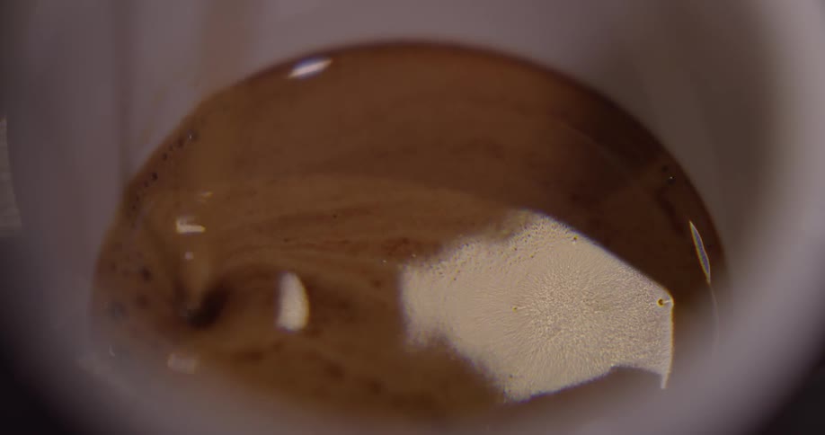 Brown liquid is poured into a white cup and light reflects off the surface