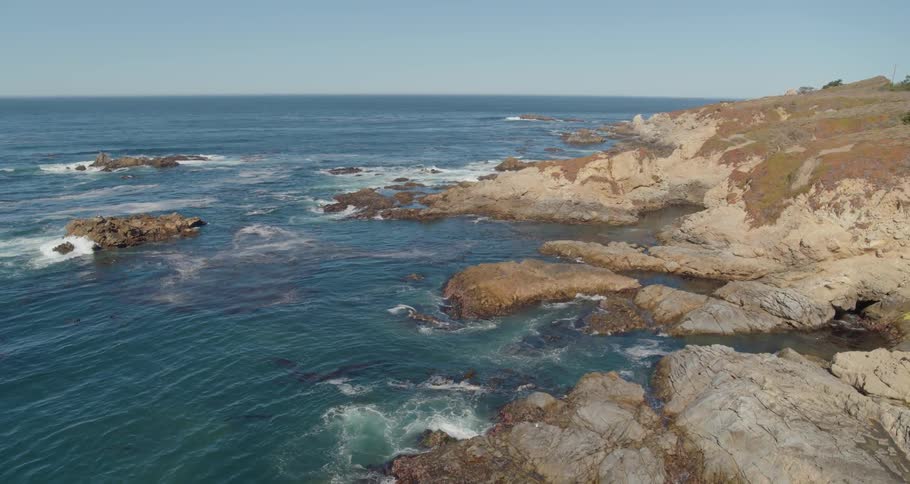 Ocean waves wash up against an incredibly rocky coastline on a sunny day with clear skies