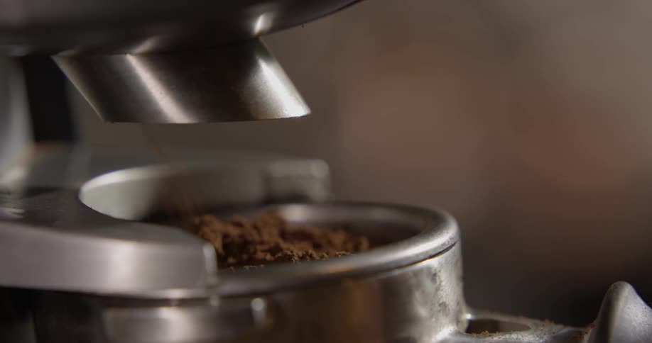 A machine spits out fresh coffee grounds into a container and the container is taken away