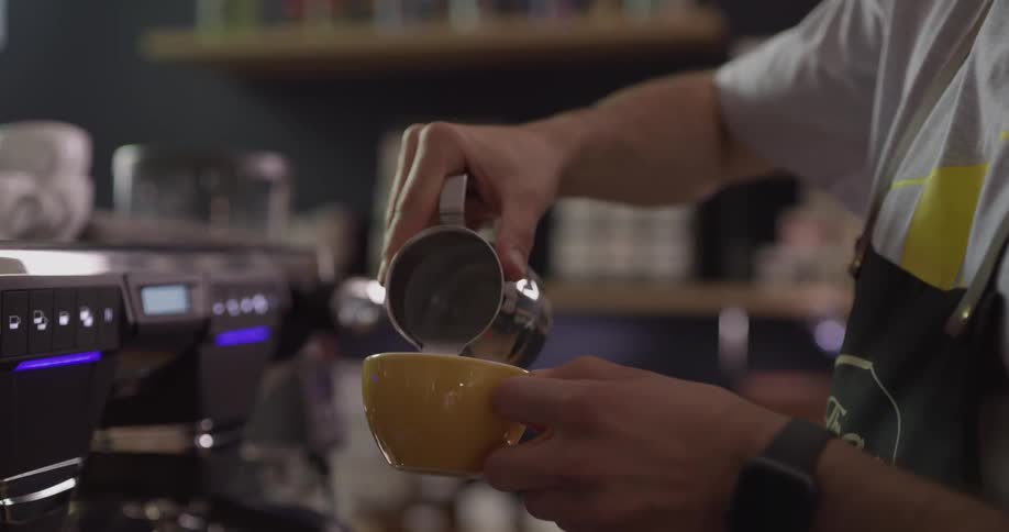 A man in an apron pouring cream into a coffee cup