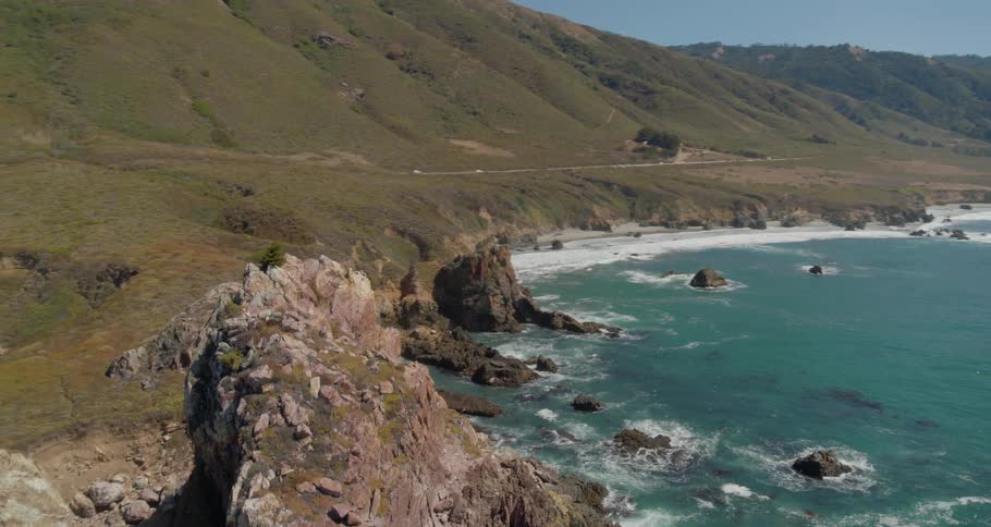 Waves crash on a rocky shore with grassy hills nearby
