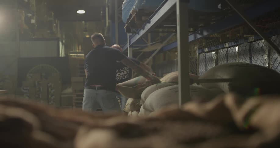 Two men picking up a heavy burlap sack of coffee beans off a shelf