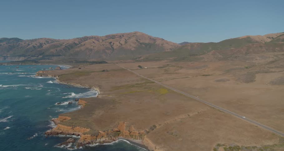 A car drives down a long road along a coast