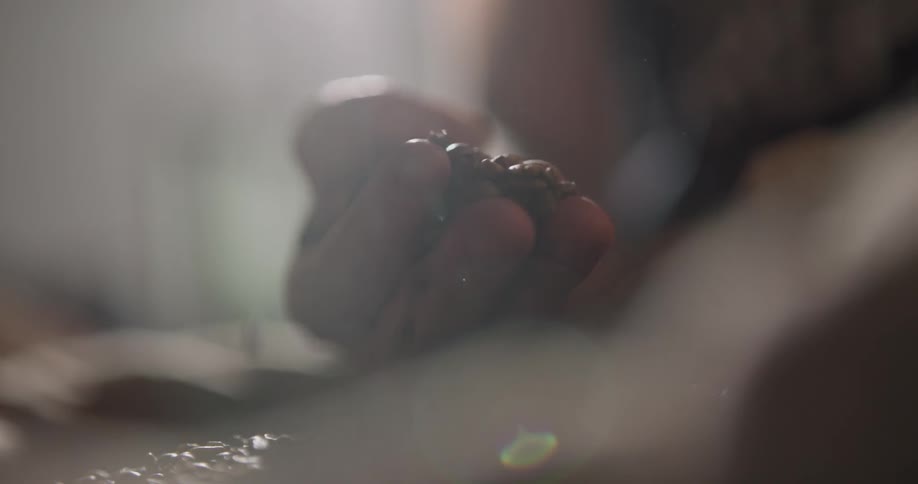 A person puts their hand in a sack of coffee beans and picks some up and lets them fall through their fingers