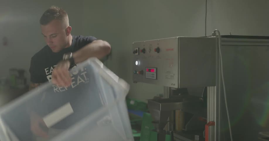 A man picks up a bin of coffee beans and dumps it in to a grinder