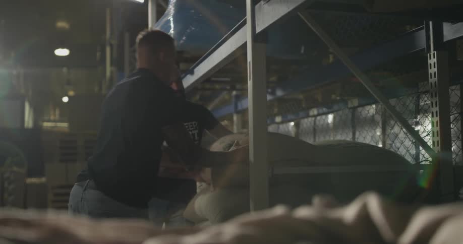 Two men carry a sack and add a to a pile