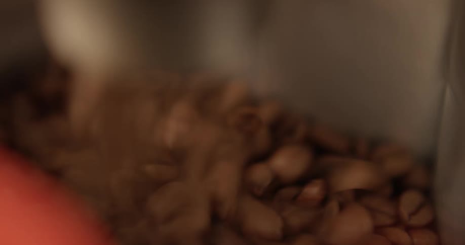 Coffee beans are quickly being poured from a metal chute to fill up a container below