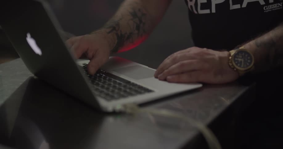 Man with a tattoo on his arm works on a laptop