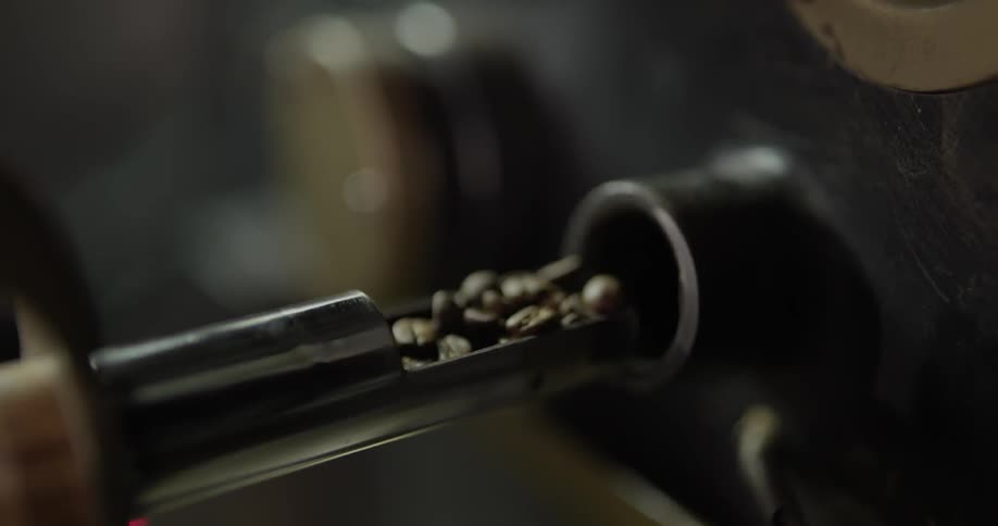 A person turns a wooden handle and removes a scoop of coffee beans from a roaster