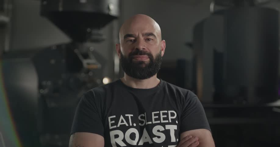 Bald bearded man stands arm crossed and looks at the camera in the workplace