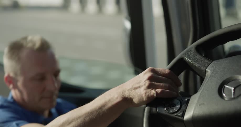 A man walks up to the door of a larger delivery truck and then opens it and climbs up into the driver seat while holding the steering wheel