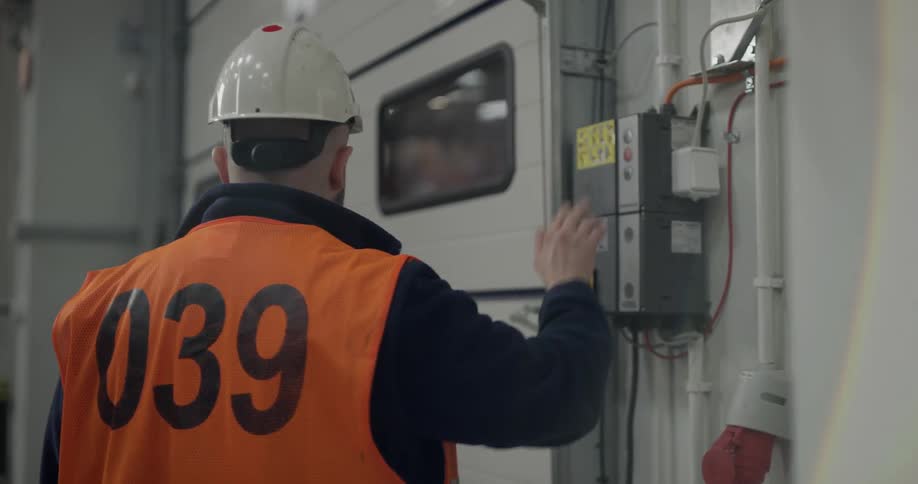 A man wearing a hard hat pushes a button to open a door
