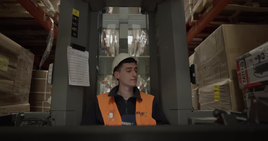 A young man drives a crane in a warehouse