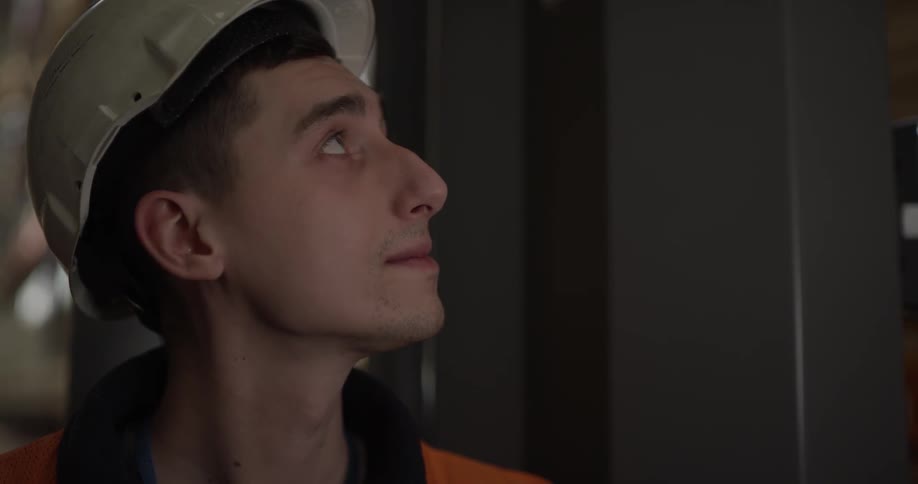 A young man in a hard hat stands and looks around