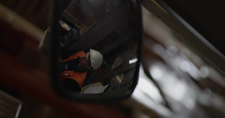 A man with a hard hat and a orange vest reflection on a rear view mirror