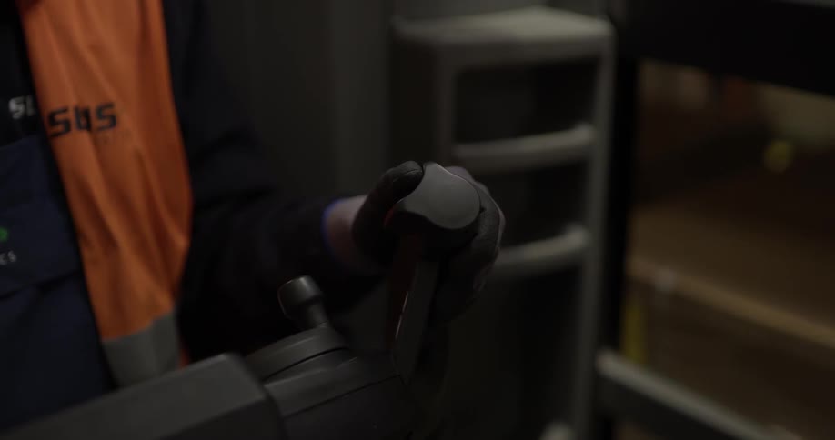 A person with an orange vest and gloves operating machinery