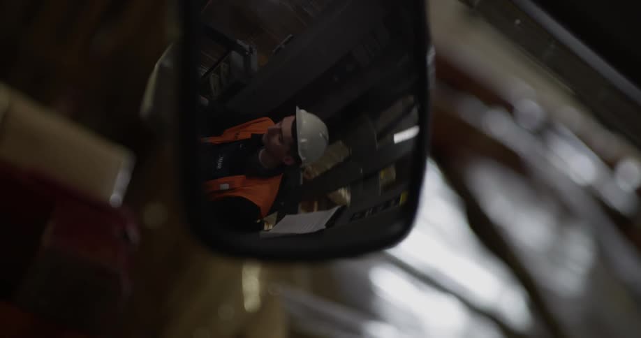 The reflection of a forklift driver in the side mirror in a warehouse